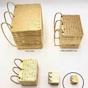 May include: A collection of gold-colored miniature notebooks, each with a unique size and design. The notebooks are bound with gold wire and feature intricate hieroglyphic patterns. Sizes range from full scale to mini doll size.
