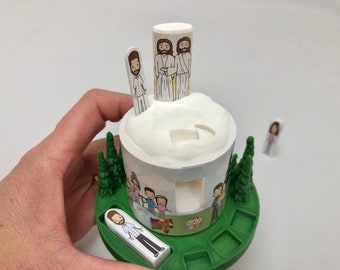 Puede incluir: Un juguete verde y blanco con un cilindro blanco en la parte superior. El cilindro tiene tres figuras en él. La base del juguete tiene un anillo verde con una ranura alrededor. Hay varias figuras en la base del juguete.