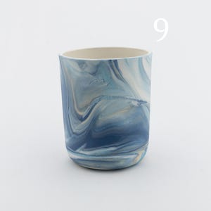 May include: A blue and white ceramic mug with a marbled design. The mug has a white interior and a rounded bottom.