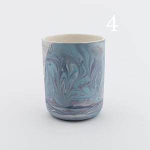 May include: A blue and white ceramic mug with a marbled design. The mug is a cylindrical shape and has a smooth, glazed finish.