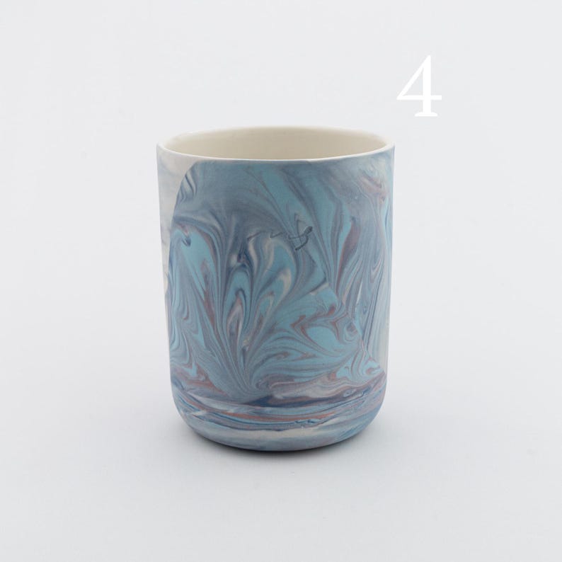 May include: A blue and white ceramic mug with a marbled design. The mug is a cylindrical shape and has a smooth, glazed finish.