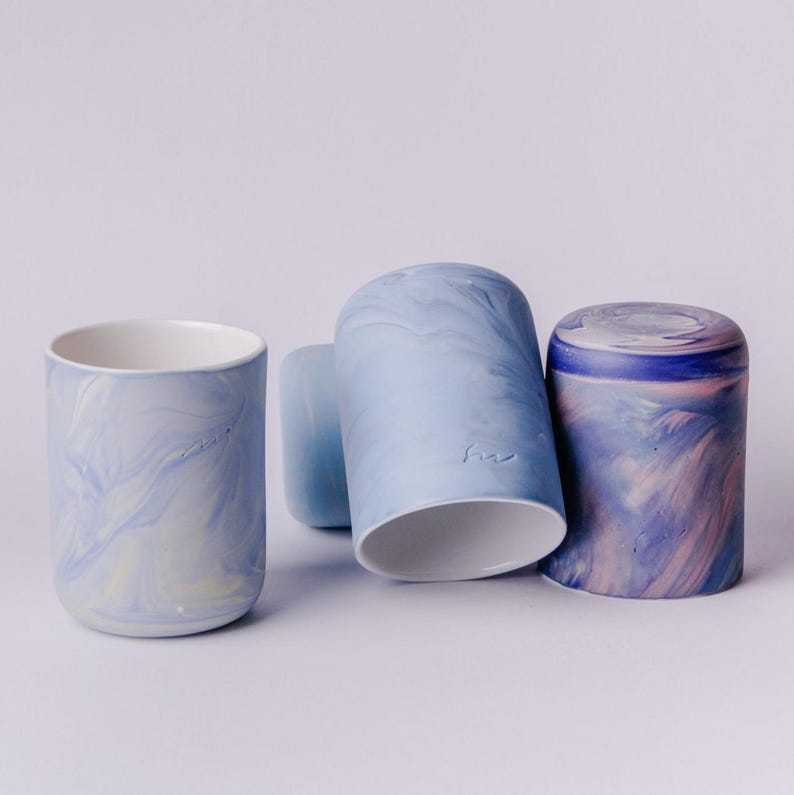 May include: Four ceramic mugs with a marbled glaze in shades of blue, white, and pink. The mugs are stacked on a white surface.