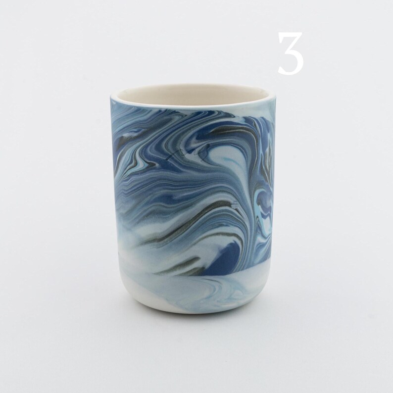 May include: A blue and white ceramic mug with a marbled design. The mug is approximately 4 inches tall.