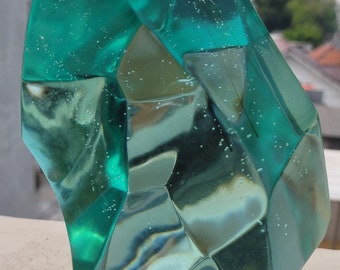 Peut inclure: Une grande sculpture en verre facetté de couleur bleu-vert avec des bulles d'air emprisonnées à l'intérieur. La sculpture a la forme d'un grand cristal irrégulier.