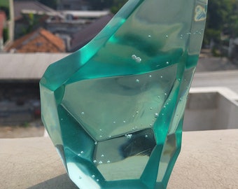 Peut inclure: Une sculpture en verre bleu turquoise avec un design géométrique facetté. La sculpture a des bulles d'air emprisonnées dans le verre.