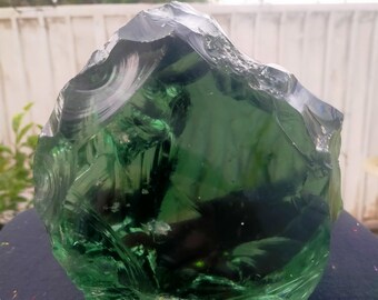 May include: A large, green, glass rock with a rough, textured surface. The rock has a translucent quality, allowing light to pass through it.