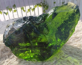 May include: A large, green, glass rock with a smooth, rounded surface. The rock has a translucent quality, allowing light to pass through it.