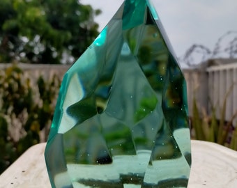 Peut inclure: Une grande sculpture en verre vert clair en forme de cristal facetté pointu. La sculpture a une surface lisse et polie et est éclairée par la lumière du soleil.