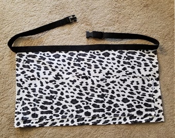 May include: A black and white leopard print apron with two pockets and an adjustable black strap with a buckle.