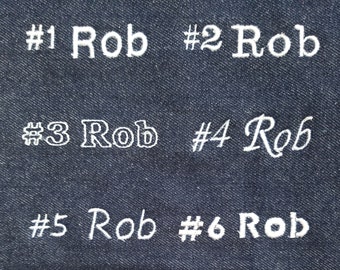 May include: Six embroidered samples of the name "Rob" on a dark blue denim fabric. Each sample is numbered from 1 to 6.