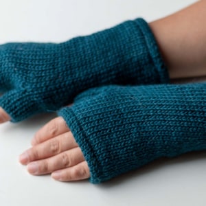 May include: A pair of teal blue knitted fingerless gloves. The gloves are made with a simple knit stitch and have a folded cuff.