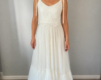 May include: A floor-length ivory dress featuring a sleeveless bodice with delicate lace detailing and thin tie-up shoulder straps. The skirt is constructed from multiple layers of sheer tulle fabric, creating a full, flowing silhouette that reaches the floor.