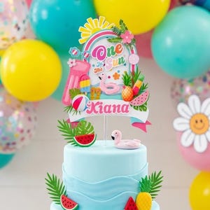 Może przedstawiać: Jasnoniebieski tort piętrowy ozdobiony elementami tropikalnymi, w tym plasterkami arbuza, ananasami i flamingiem. Tort zwieńczony jest banerem z napisem "One in the Sun" i imieniem "Kiana". Kolorowe balony w kolorze różowym, żółtym i turkusowym w tle.