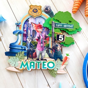 Op de afbeelding: Een kleurrijke Zootopia-taarttopper met Nick Wilde, Judy Hopps en andere personages. De topper bevat de tekst "HAPPY BIRTHDAY" en "MATEO", met een nummer 5. Het ontwerp bevat een politielogo en een straatnaambord.