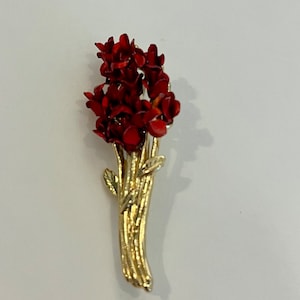 May include: A gold-toned metal brooch in the shape of a bouquet of flowers. The flowers are a deep red color, with detailed petals. The stems are gold, with small green leaves. The brooch is a vintage style.