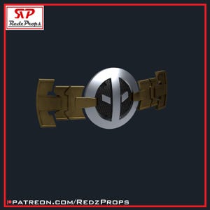 May include: A silver and gold belt buckle with a Deadpool logo. The logo is a black and white design with a red outline. The buckle is made of metal and has a textured surface.