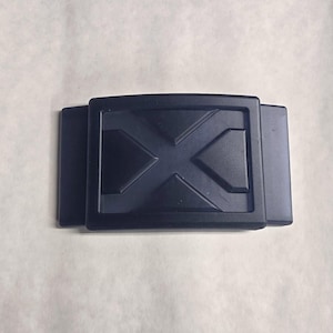 May include: A black plastic belt buckle with a raised X design.