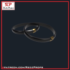 May include: Two black rings with gold accents. The rings are interlocked and appear to be made of a smooth, polished material.