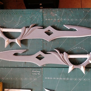 May include: Two gray foam swords with intricate designs. The swords have a diamond-shaped cutout in the middle and a white foam handle.