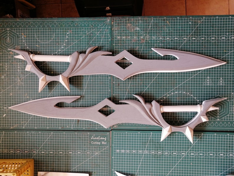 May include: Two gray foam swords with intricate designs. The swords have a diamond-shaped cutout in the middle and a white foam handle.