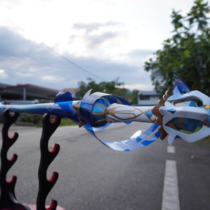 Peut inclure: Une &eacute;p&eacute;e d&eacute;corative bleue et blanche avec des accents dor&eacute;s, expos&eacute;e sur un support d'&eacute;p&eacute;e noir. L'&eacute;p&eacute;e pr&eacute;sente un design d&eacute;taill&eacute; avec des sculptures complexes et une pointe pointue.