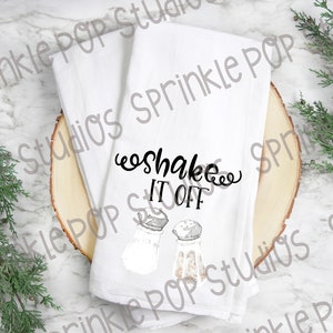 May include: White kitchen towel with the text "Shake It Off" in black cursive lettering. Two salt shakers are depicted below the text.