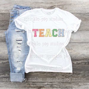 Könnte beinhalten: Weißes T-Shirt mit dem Wort "TEACH" in Regenbogenfarben mit goldenen Glitzerakzenten. Die Buchstaben sind in einer Schriftart im College-Stil.