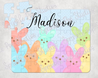 Puede incluir: Un rompecabezas personalizado con un fondo azul con lunares blancos. El nombre "Madison" está escrito en cursiva negra. Las piezas del rompecabezas tienen forma de conejos de malvavisco Peeps de colores pastel.
