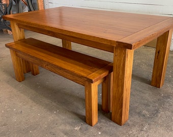 May include: A wooden table and bench set in a natural wood finish. The table has a rectangular top and four legs. The bench has a rectangular seat and four legs.