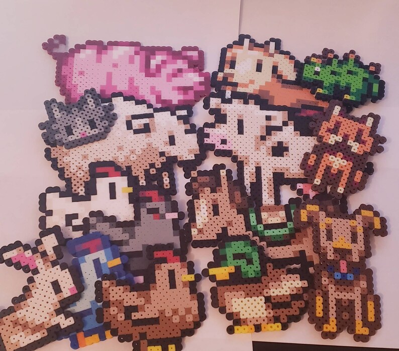 May include: A collection of pixel art farm animals, including a pink pig, a gray cat, a white cow, a brown dog, a duck, a chicken, and a rabbit. The animals are made from colorful plastic beads.