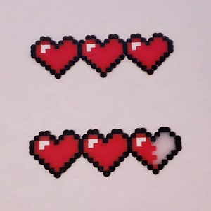 Puede incluir: Dos filas de corazones rojos pixelados, cada fila con tres corazones. La fila superior tiene tres corazones completos, mientras que la fila inferior tiene dos corazones completos y un coraz&oacute;n parcialmente lleno.