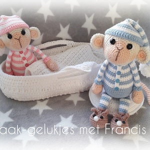 Op de afbeelding: Twee gehaakte aapjes die pyjama's en slaapmutsen dragen. Het roze aapje zit in een witte gehaakte mand. Het blauwe aapje zit op een grijs en wit gestreepte deken met sterren. De tekst "Haak-gelukjes met Francis" staat onderaan de afbeelding.