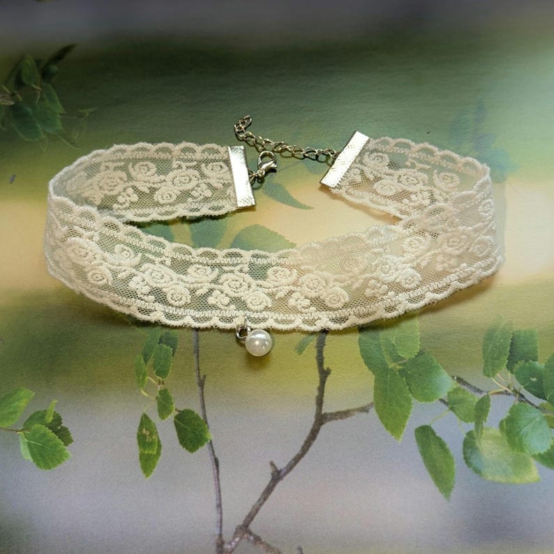 Pu&ograve; includere: Girocollo in pizzo color avorio con motivo floreale e piccolo pendente a perla. Il girocollo ha una catena e una chiusura color argento. Il design delicato &egrave; adatto per occasioni speciali o per l'uso quotidiano.