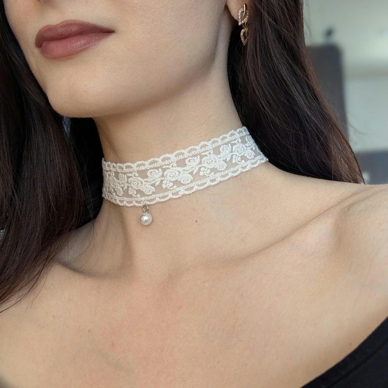 Pu&ograve; includere: Una collana girocollo in pizzo bianco con un motivo floreale e un piccolo pendente di perla. La delicata collana &egrave; indossata intorno al collo. Il choker &egrave; un accessorio elegante.