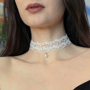 Pu&ograve; includere: Una delicata collana girocollo in pizzo bianco con un design floreale e un piccolo pendente di perla. La collana &egrave; realizzata con due strati di pizzo e si indossa intorno al collo.
