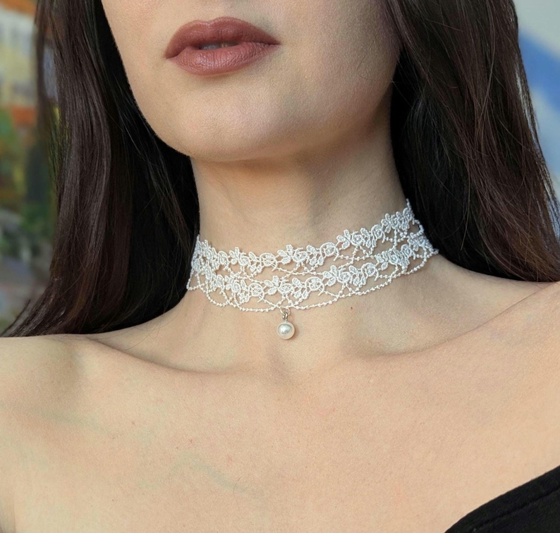 Pu&ograve; includere: Una delicata collana girocollo in pizzo bianco con un design floreale e un piccolo pendente di perla. La collana &egrave; realizzata con due strati di pizzo e si indossa intorno al collo.