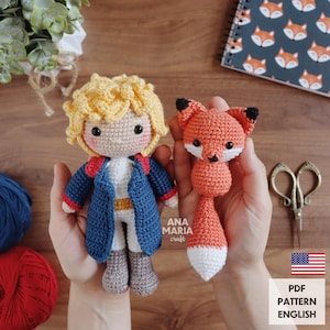 Puede incluir: Muñeco de ganchillo de un niño con chaqueta azul con ribetes rojos y un zorro de ganchillo. El muñeco tiene pelo rubio y lleva una camisa blanca. El zorro es naranja con vientre y punta de la cola blancos. Incluye el texto "ANA MARIA craft" y "PDF PATTERN ENGLISH".