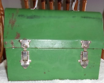 May include: A vintage green metal lunch box with two silver clasps. The lunch box has a slightly rounded top and is showing signs of wear.