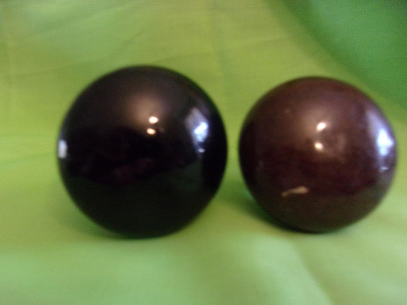 Może przedstawiać: Dwa gładkie, okrągłe ozdoby. Jedna jest czarna, a druga ciemnobrązowa.