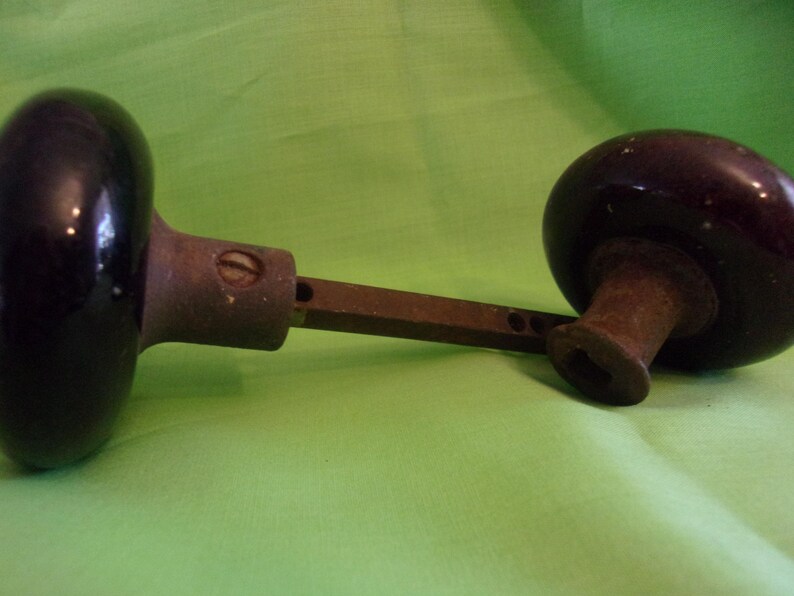 Może przedstawiać: Antyczny gałka drzwiowa z czarnym ceramicznym wykończeniem i metalowym trzpieniem. Gałka jest przymocowana do metalowego pręta.