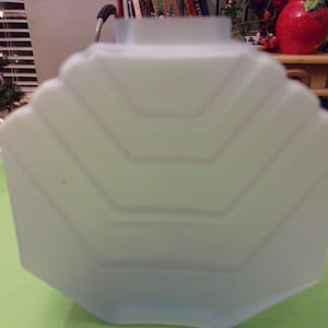 May include: A pale blue, geometric-shaped glass lampshade. The shade has a scalloped edge and a series of horizontal lines that create a layered effect. The lampshade is sitting on a green surface.