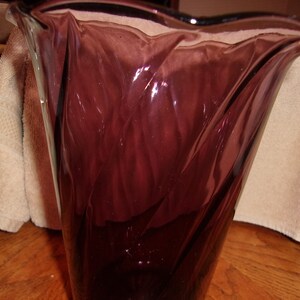 May include: A tall, clear glass vase with a swirling, textured design. The vase is a deep purple color.