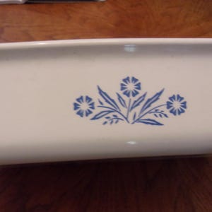 May include: A rectangular, off-white baking dish with a blue floral design. The blue design features three flower clusters with leaves. The dish is made of a durable material, suitable for oven use.