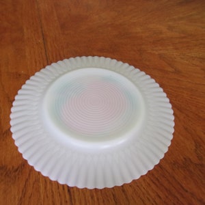 May include: White milk glass plate with a scalloped edge and a pink and blue swirl design on the bottom.