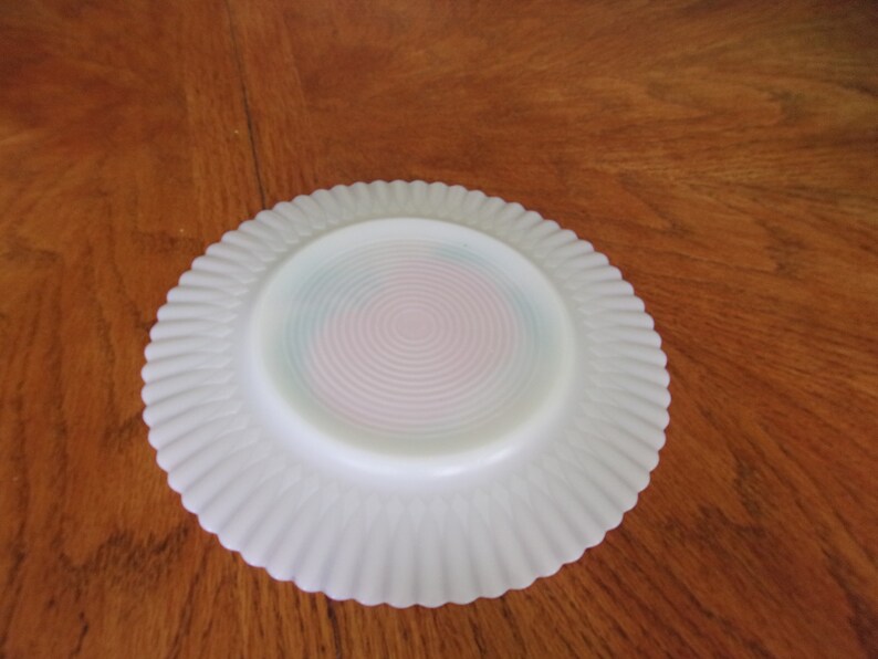 May include: White milk glass plate with a scalloped edge and a pink and blue swirl design on the bottom.