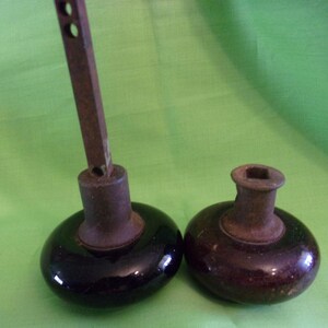 Może przedstawiać: Dwa antyczne gałki drzwiowe z metalowymi trzpieniami i czarnymi i brązowymi ceramicznymi podstawami.