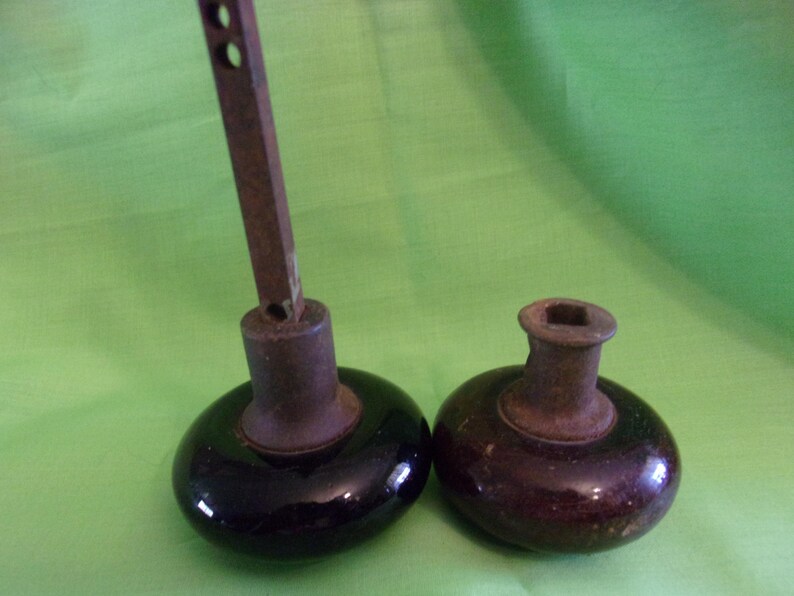 Może przedstawiać: Dwa antyczne gałki drzwiowe z metalowymi trzpieniami i czarnymi i brązowymi ceramicznymi podstawami.