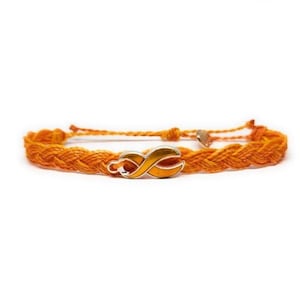 May include: Orange braided bracelet featuring a silver and orange ribbon charm. The bracelet is made of woven orange threads and has a small heart-shaped detail near the clasp. A simple and elegant accessory.