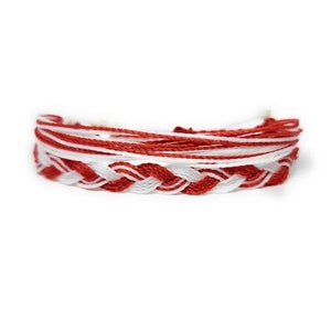 Peut inclure: Bracelet d'amitié tressé rouge et blanc. Le bracelet est composé de plusieurs fils de fil tissés ensemble dans un motif.