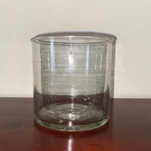 K&ouml;nnte beinhalten: Ein klarer, zylindrischer Glasbeh&auml;lter mit einer weiten &Ouml;ffnung. Der Beh&auml;lter besteht aus transparentem Glas und steht auf einer dunklen Holzoberfl&auml;che. Der Beh&auml;lter ist leer und scheint ein dekorativer oder Aufbewahrungsbeh&auml;lter zu sein.